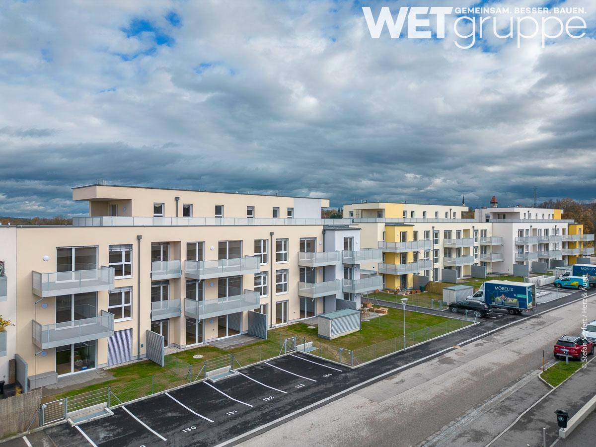 Weitläufige Wohnanlage mit modernen Gebäuden, Balkonen und Parkplätzen unter bewölktem Himmel.