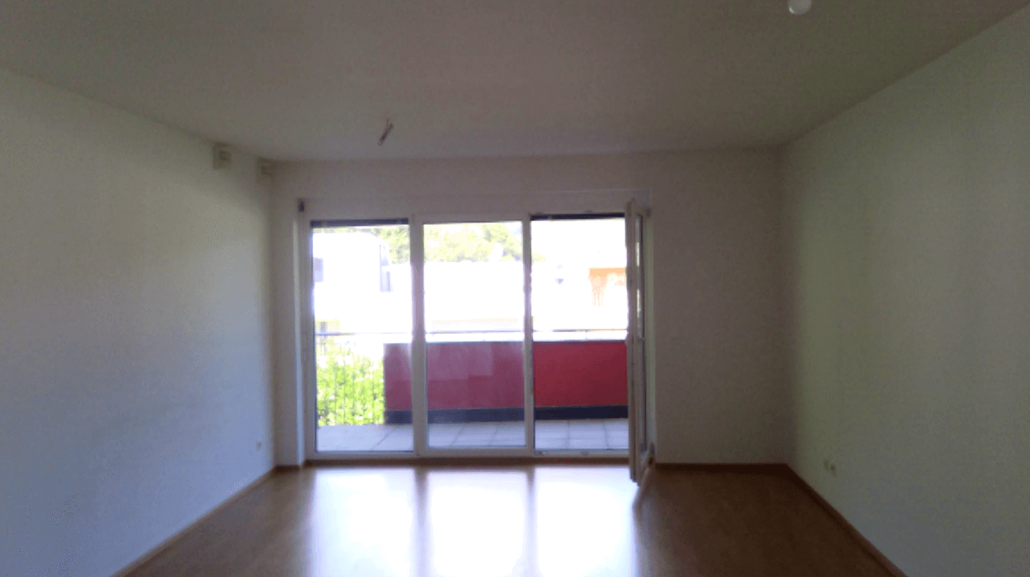 Heller, leerer Wohnraum mit Laminatboden und großem Fenster mit Zugang zum Balkon.