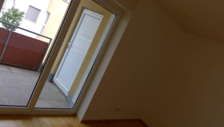 Heller Innenraum mit Holzboden und Zugang zu einem Balkon oder einer Loggia.