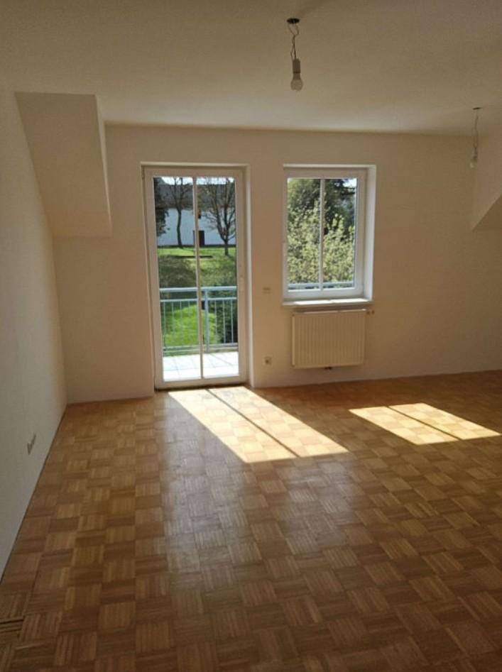 Lichtdurchflutetes Zimmer mit Parkettboden, Balkonzugang und großem Fenster.