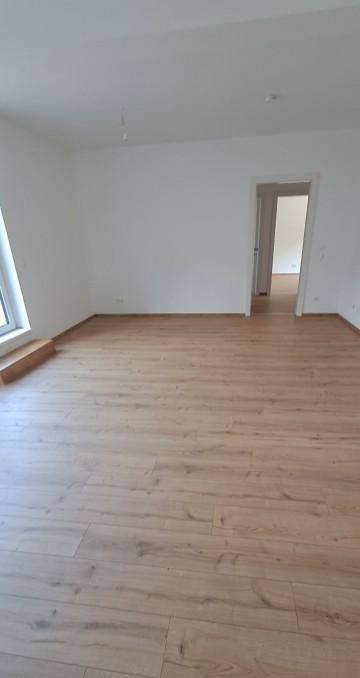 Heller, leerer Raum mit modernem Laminatboden und weißen Wänden, bereit zum Einzug.