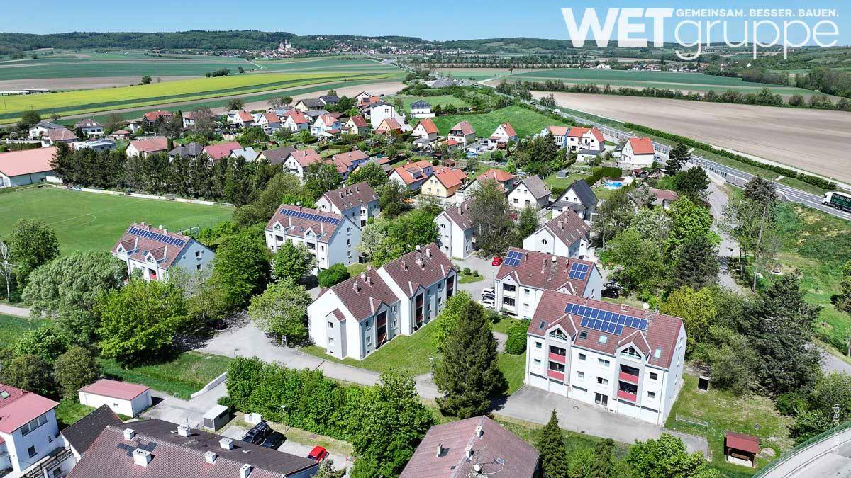 Weitläufige Luftaufnahme einer Wohnsiedlung, umgeben von grünen Feldern und ländlicher Landschaft.