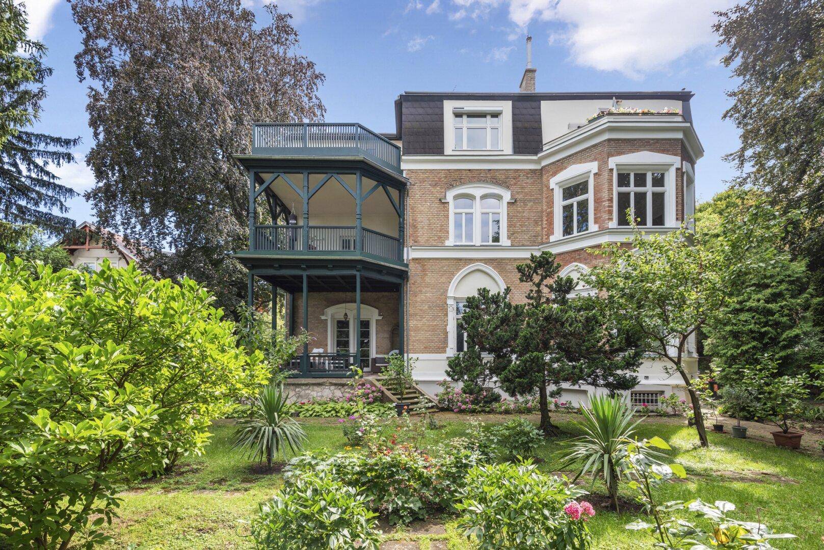 Elegante Stadtvilla mit klassischer Backsteinfassade, großem Garten und mehrstöckigem Balkon-Loggia-Anbau.