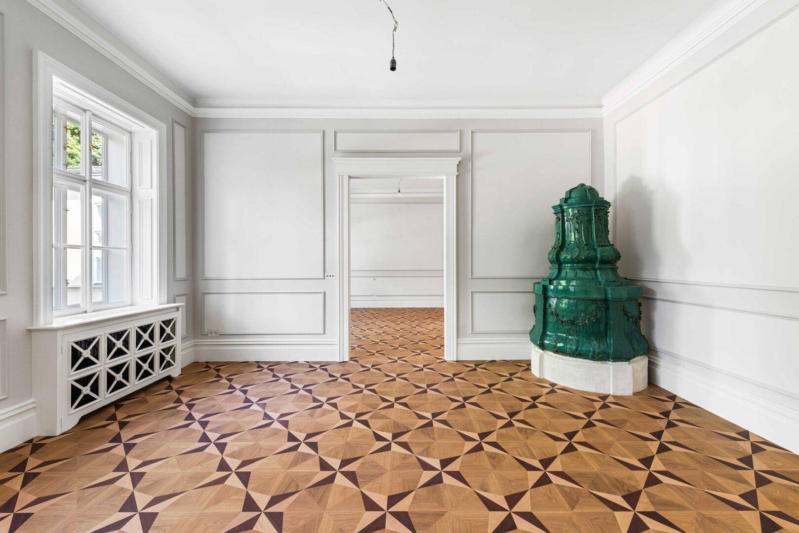 Eleganter Raum mit grünem Kachelofen, kunstvollem Parkettboden und hohen Decken.