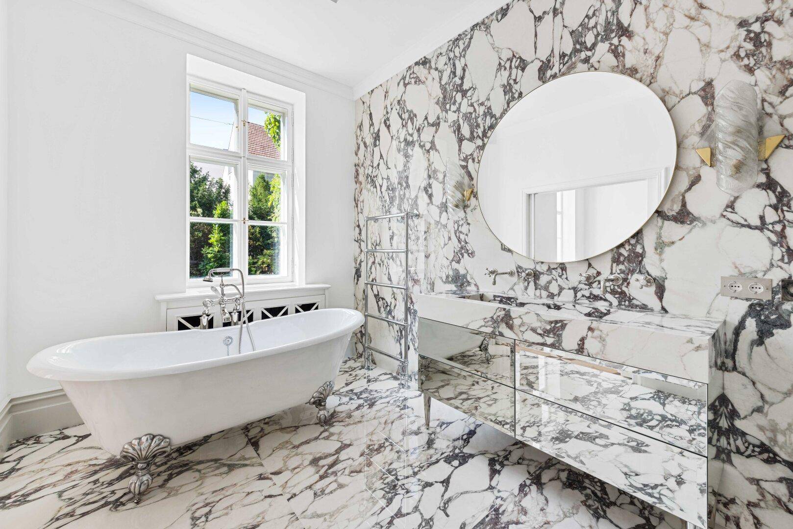 Luxuriöses Badezimmer mit freistehender Badewanne, Marmorwänden und großem Fenster.