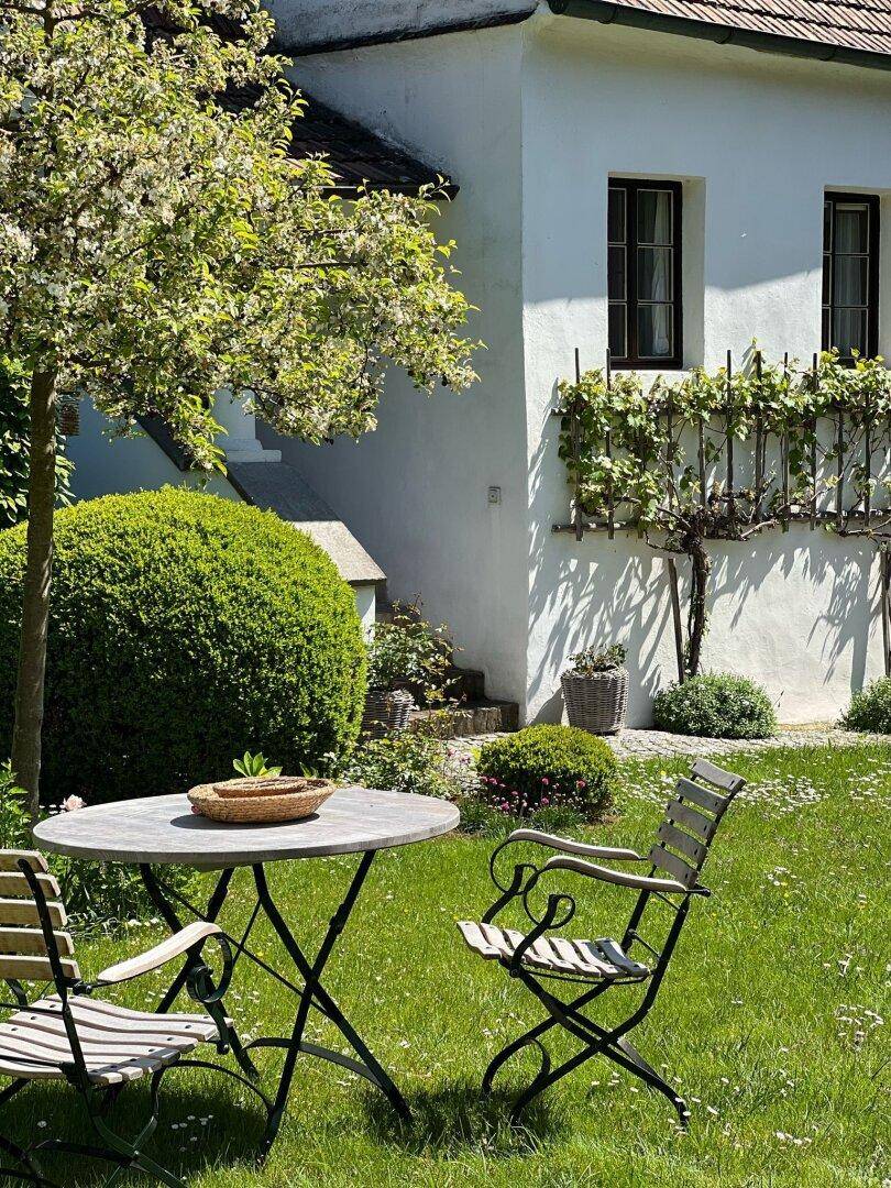 Gemütlicher Sitzbereich im Garten mit Tisch und Stühlen vor der historischen Hausfassade.