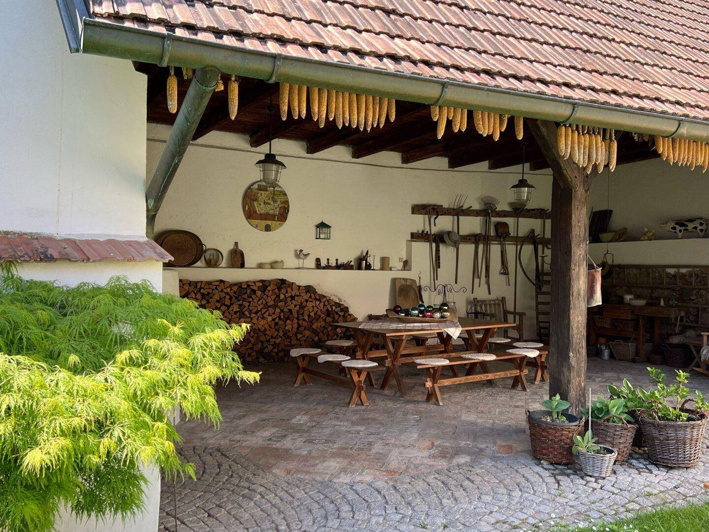 Rustikaler überdachter Außenbereich mit großem Holztisch und Bänken, ideal für gesellige Runden.