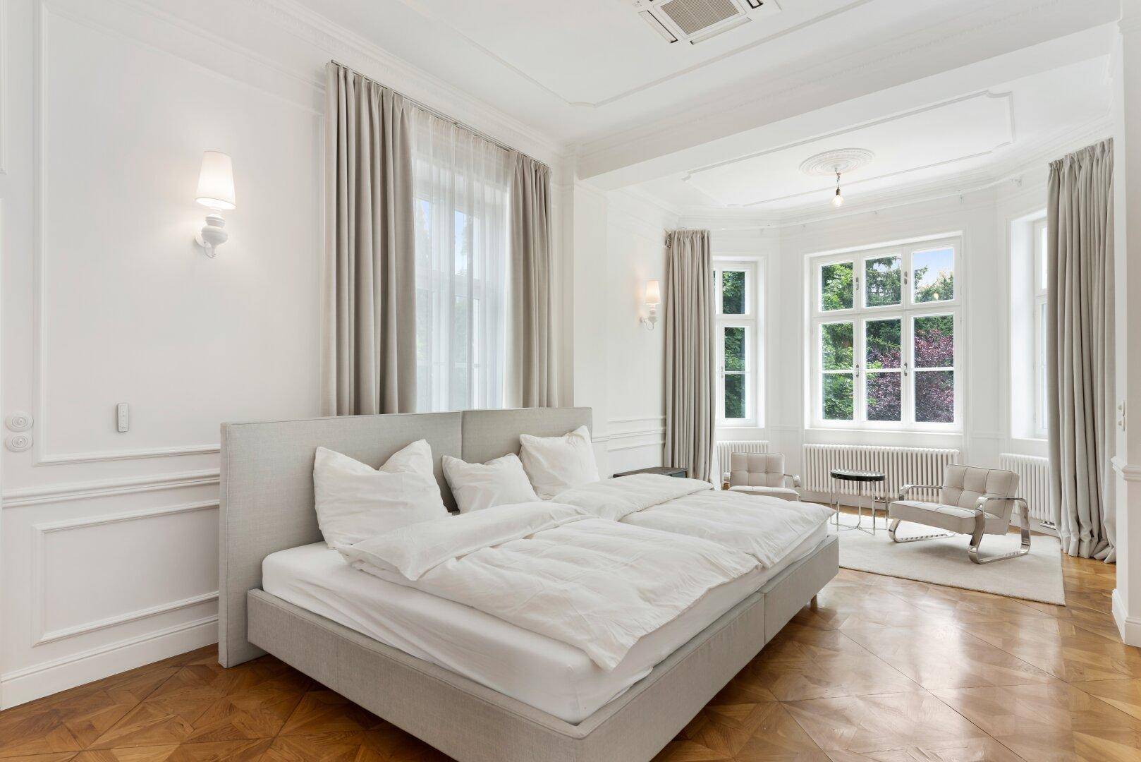 Helles Schlafzimmer mit großem Doppelbett, bequemen Sesseln und viel Tageslicht.