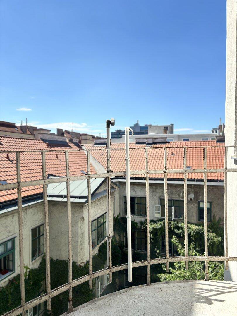 Balkon mit Metallgeländer und Blick über die Dächer der Stadt unter blauem Himmel.