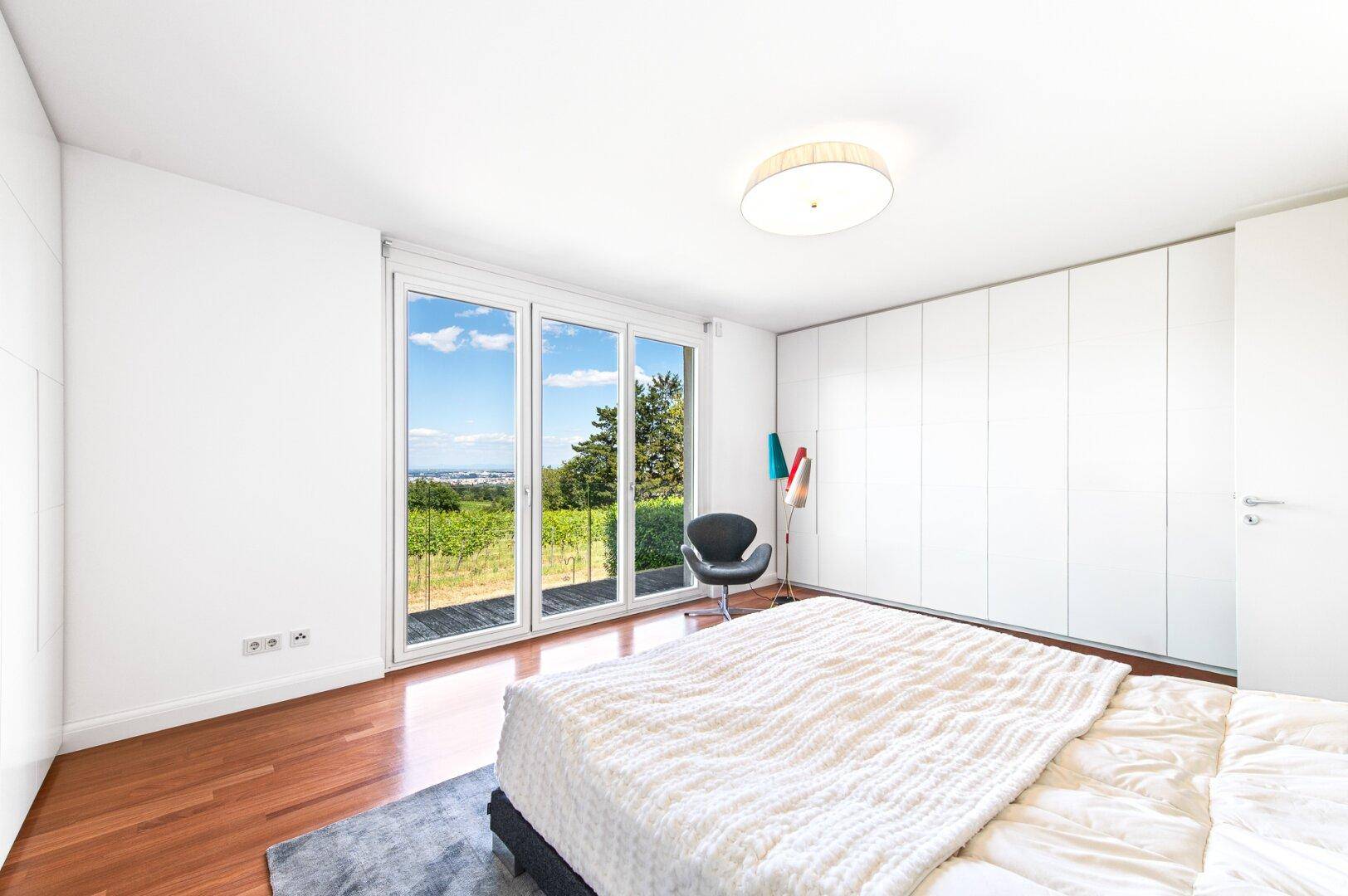 Schlafzimmer mit großen Fenstern, Holzboden und weitem Blick auf Weinberge und Landschaft.