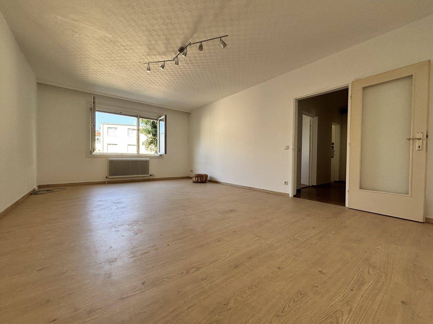 Geräumiges, helles Wohnzimmer mit Laminatboden und Zugang zu weiteren Räumen.
