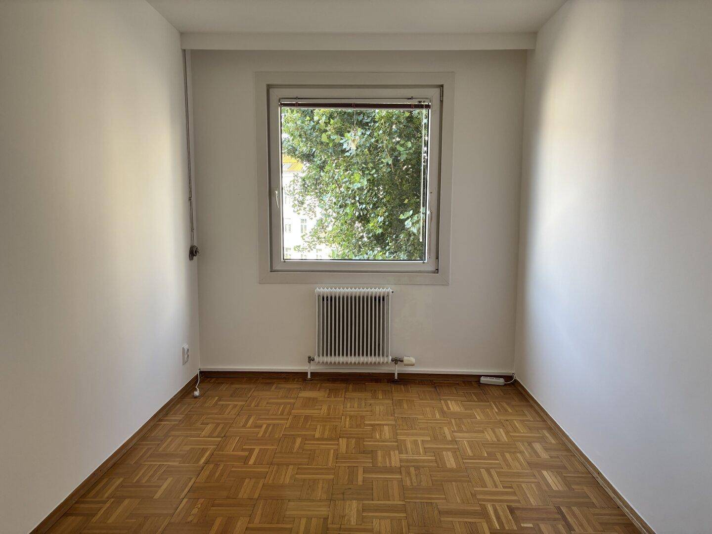 Kleines, helles Zimmer mit Parkettboden und Blick ins Grüne.