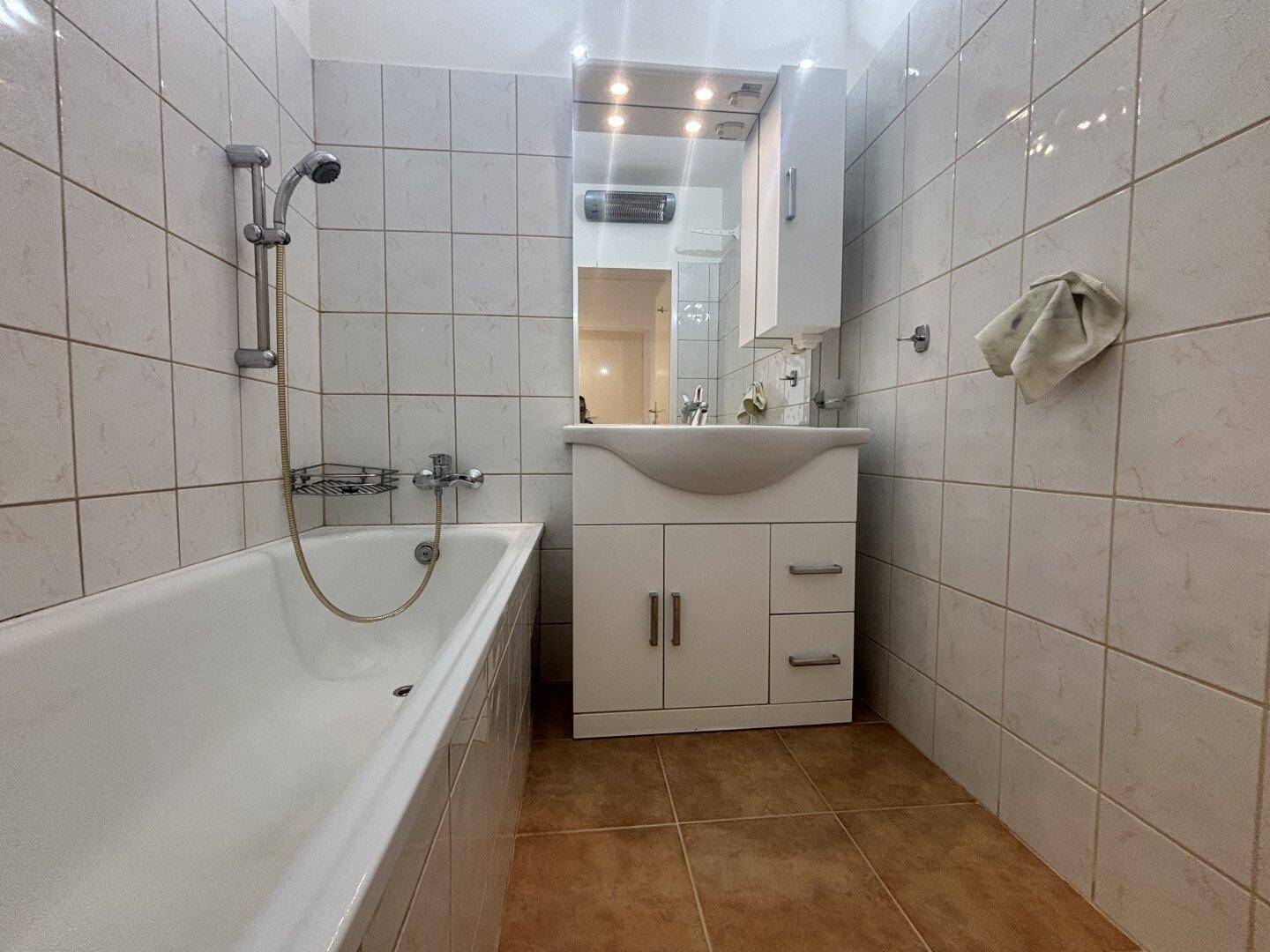 Gefliestes Badezimmer mit Badewanne, Waschbecken und Spiegelschrank.