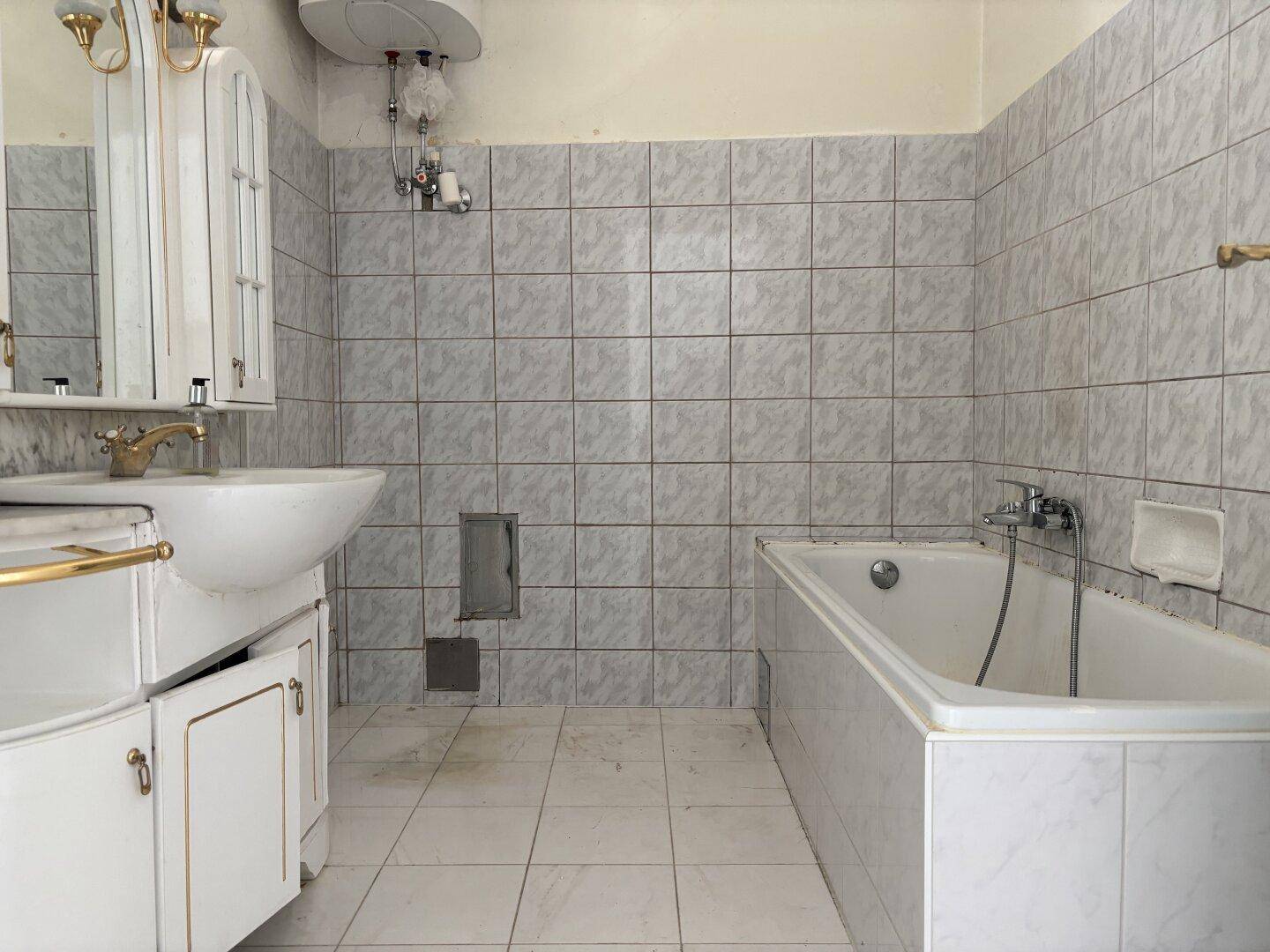 Badezimmer mit hellgrauen Fliesen, einer Badewanne und einem Waschtisch mit Spiegelschrank.