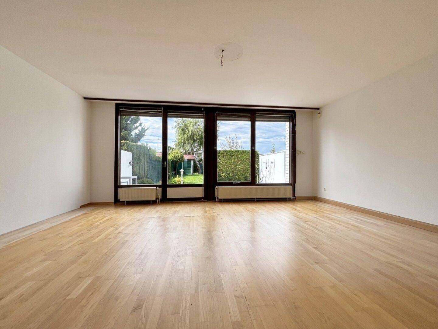 Helles Wohnzimmer mit großen Fenstern, Parkettboden und Blick in den Garten.