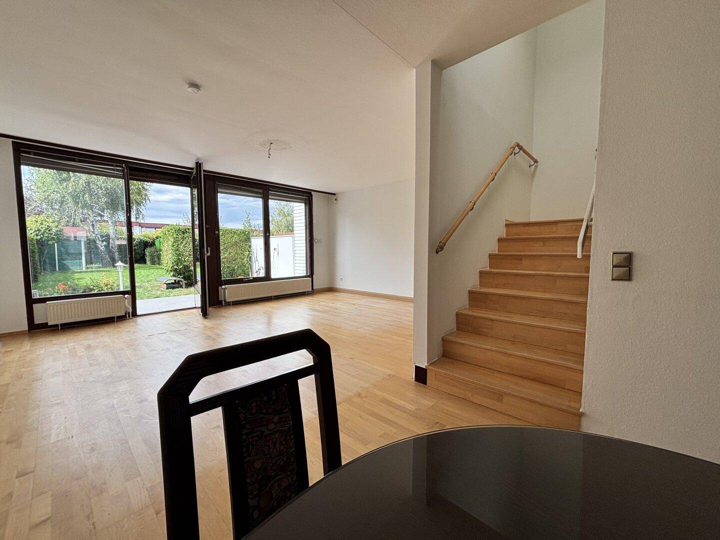 Heller Wohnbereich mit Holztreppe und großen Fenstern zum Garten.