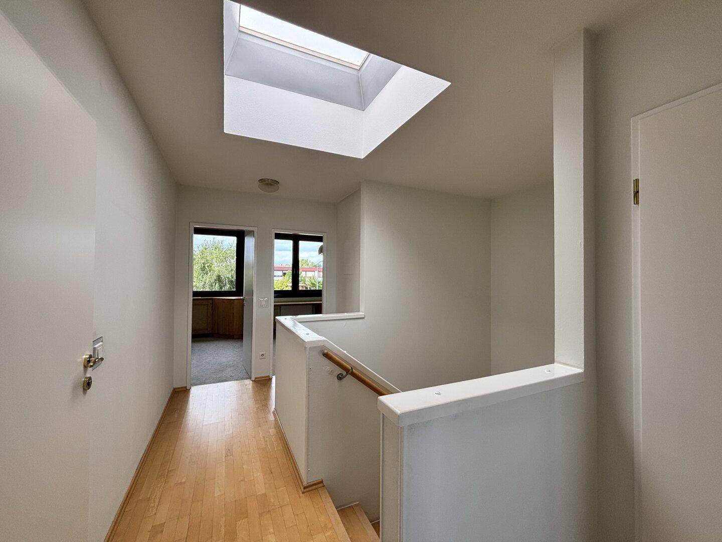 Heller Flur im Obergeschoss mit Holztreppe und einem Dachfenster für natürliches Licht.