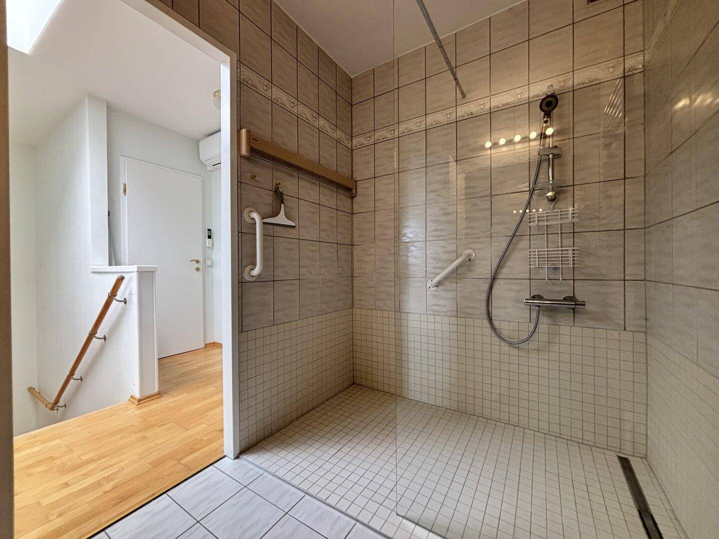 Modernes Badezimmer mit ebenerdiger Dusche, Fliesen und Haltegriffen.