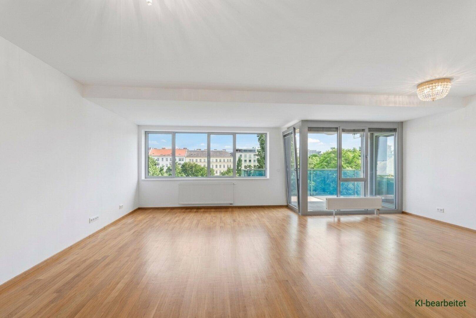 Helles, leeres Wohnzimmer mit großen Fenstern, Holzboden und Zugang zu einem Balkon.