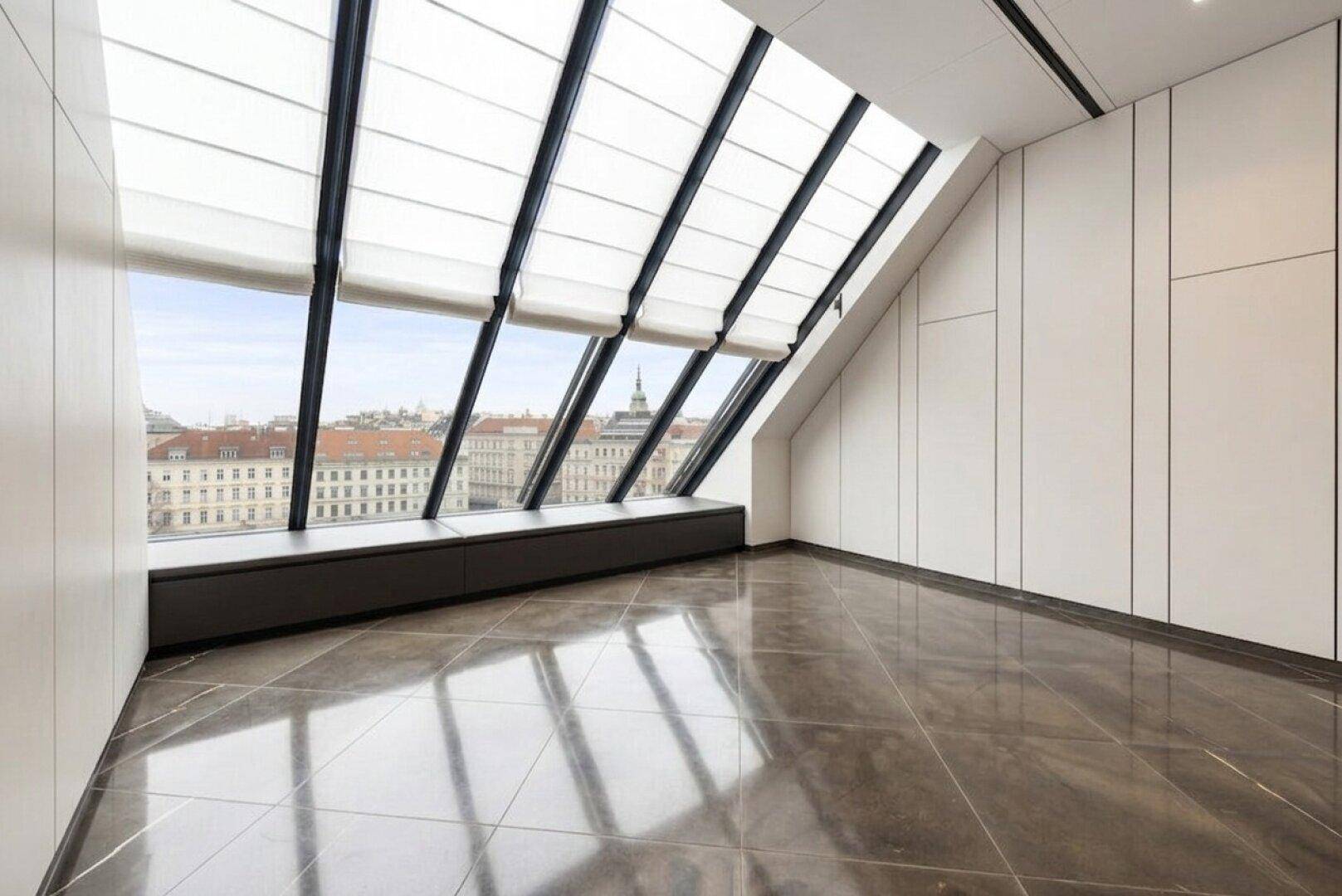 Moderner Raum mit dunklem Fliesenboden, schrägen Fenstern und Panoramablick über die Stadt.