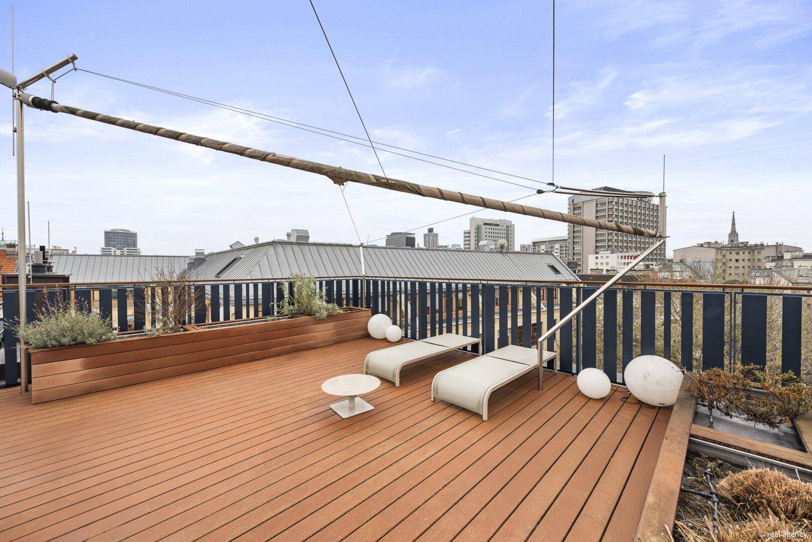 Geräumige Dachterrasse mit Holzdeck, Liegestühlen und weitem Blick über die Stadt.