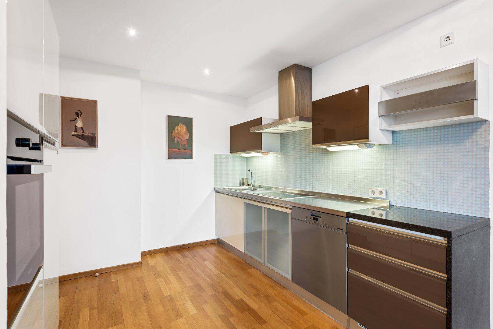 Moderne Einbauküche mit glänzenden Fronten, dunkler Arbeitsplatte und integrierten Geräten.