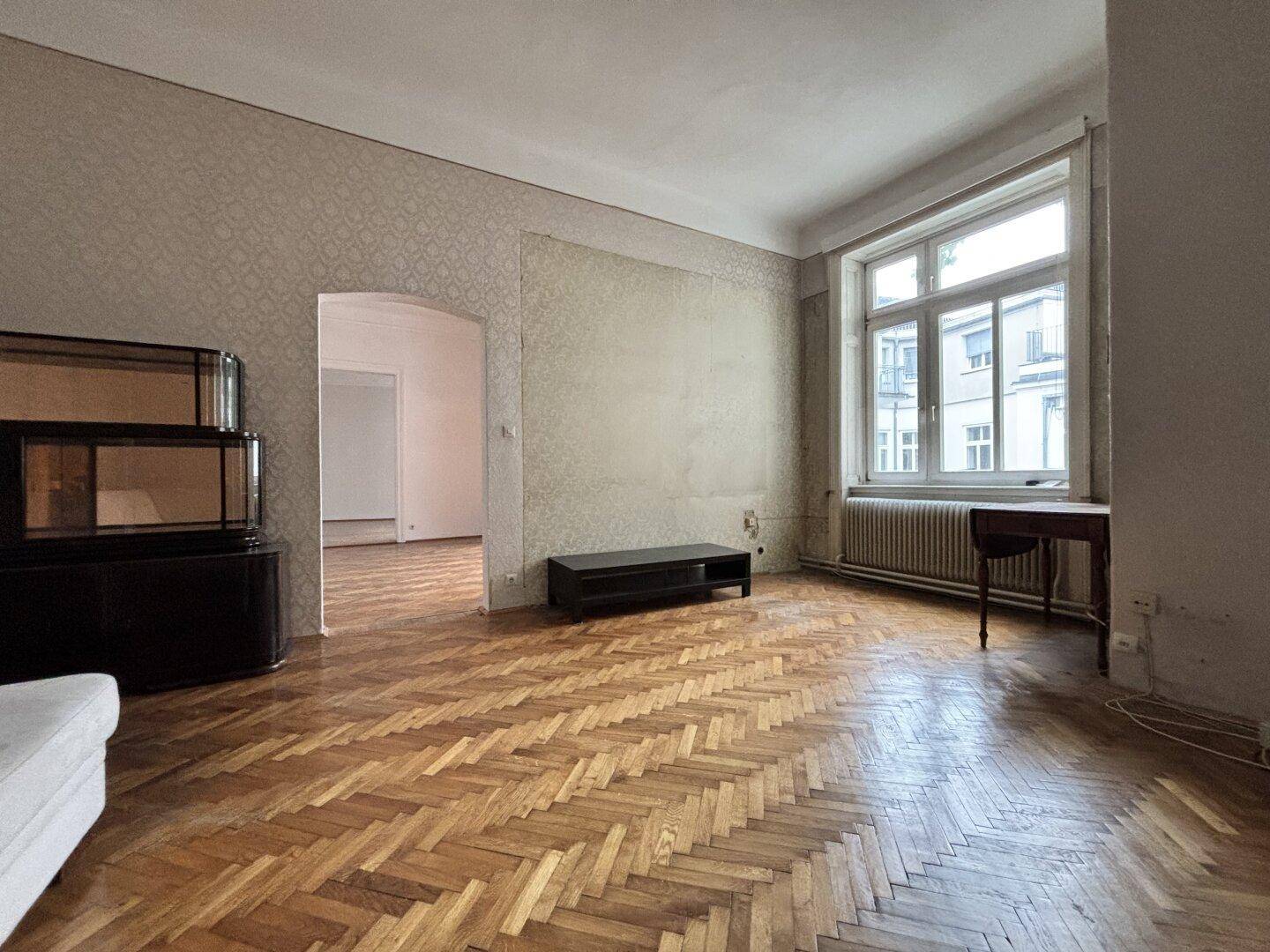 Helles Wohnzimmer mit klassischem Fischgrätparkett und einem großen Fenster, das den Raum mit Licht füllt.