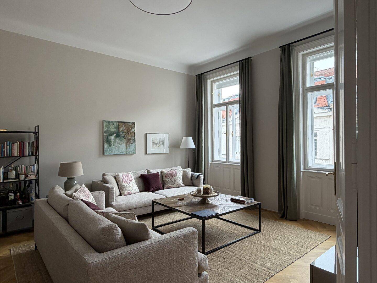 Geräumiges Wohnzimmer mit beigen Sofas, Holzboden und hohen Fenstern.