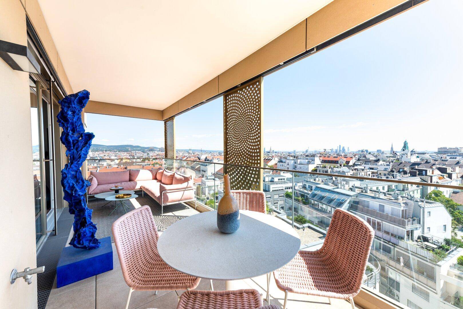Geräumiger Balkon mit modernen Sitzgelegenheiten, Kunstobjekt und weitem Stadtblick.