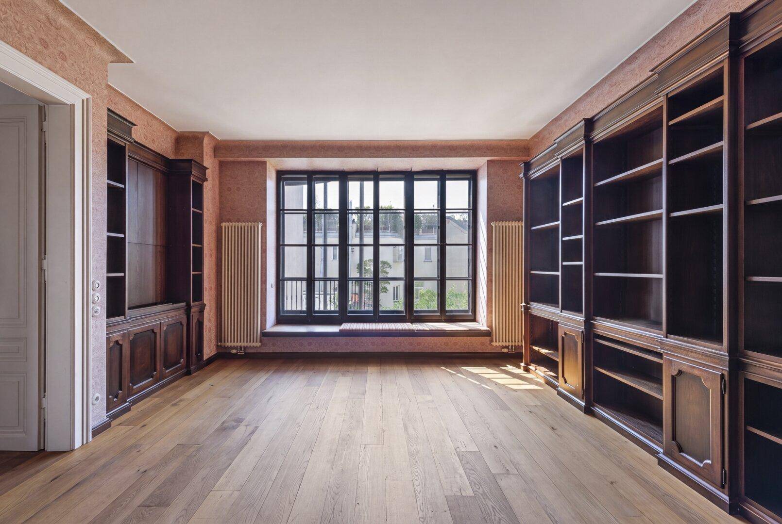 Elegantes Arbeitszimmer mit raumhohen Holzregalen, breiten Dielen und großem Fenster.
