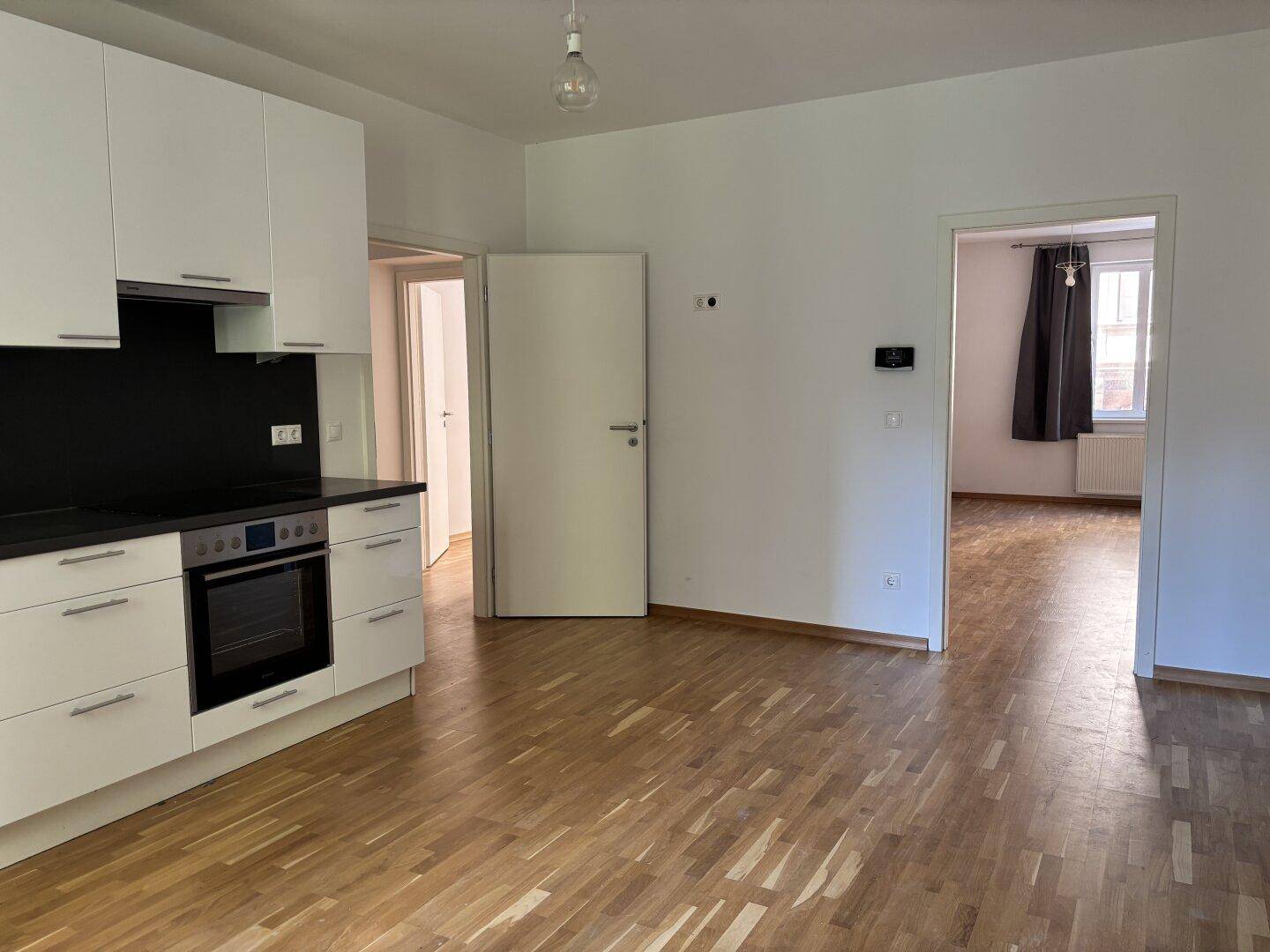 Heller Küchenbereich mit Holzboden und offenem Zugang zu angrenzenden Zimmern.