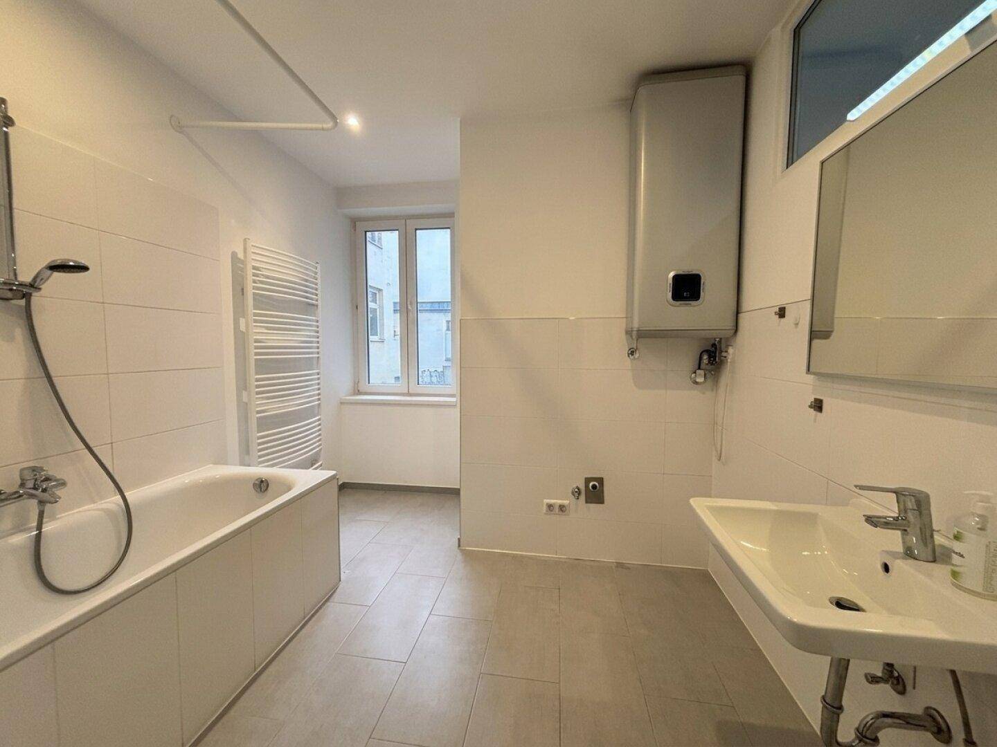 Modernes Badezimmer mit Badewanne, Waschbecken, beheiztem Handtuchhalter und Fenster.