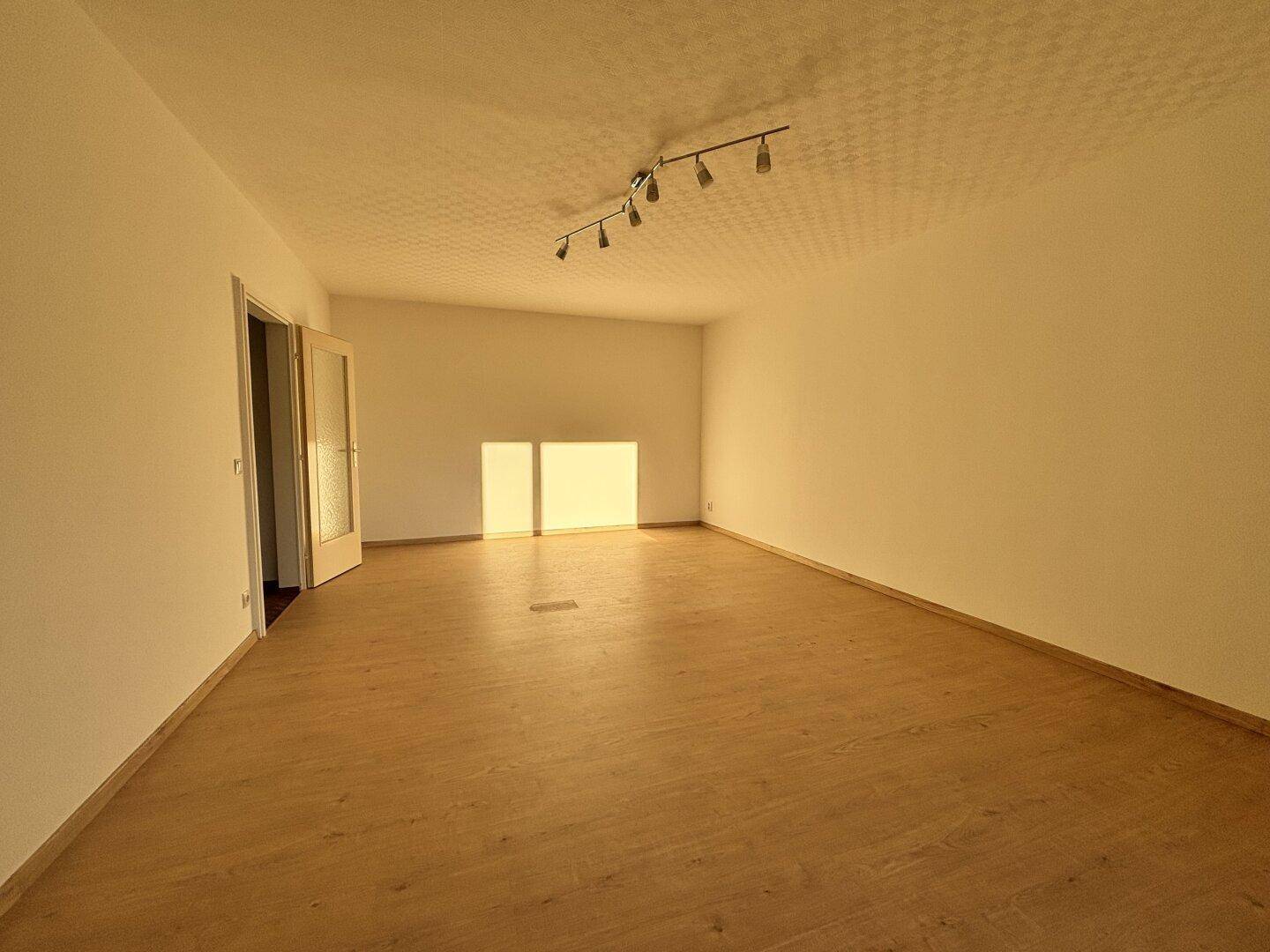 Geräumiges, leeres Zimmer mit Laminatboden und viel natürlichem Lichteinfall.