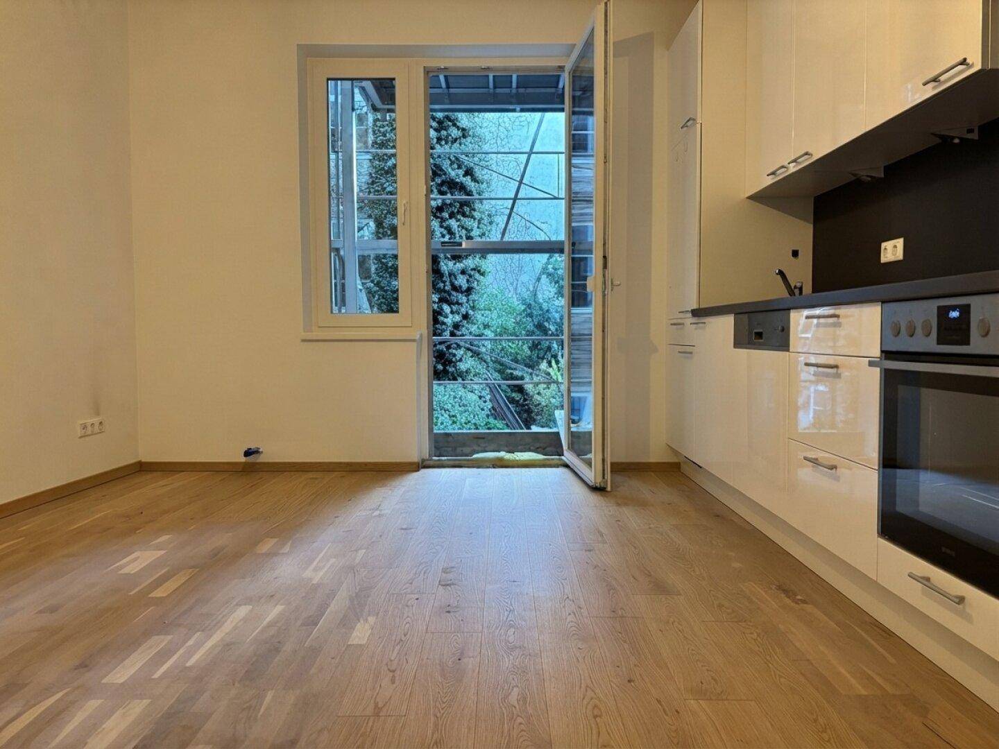 Moderne Küche mit weißen Hochglanzschränken, integriertem Backofen und Zugang zu einem grünen Außenbereich.
