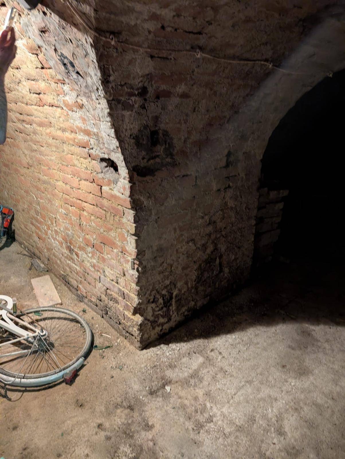 Gewölbter Kellerraum mit Ziegelwänden und einem Fahrrad, das an der Wand lehnt.