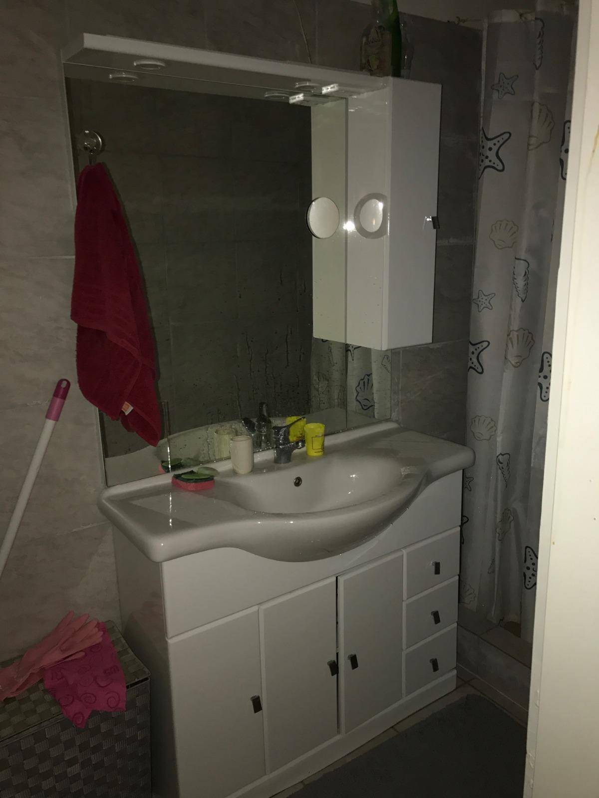 Badezimmer mit Waschbecken, Spiegelschrank und Duschvorhang in neutralen Fliesenfarben.