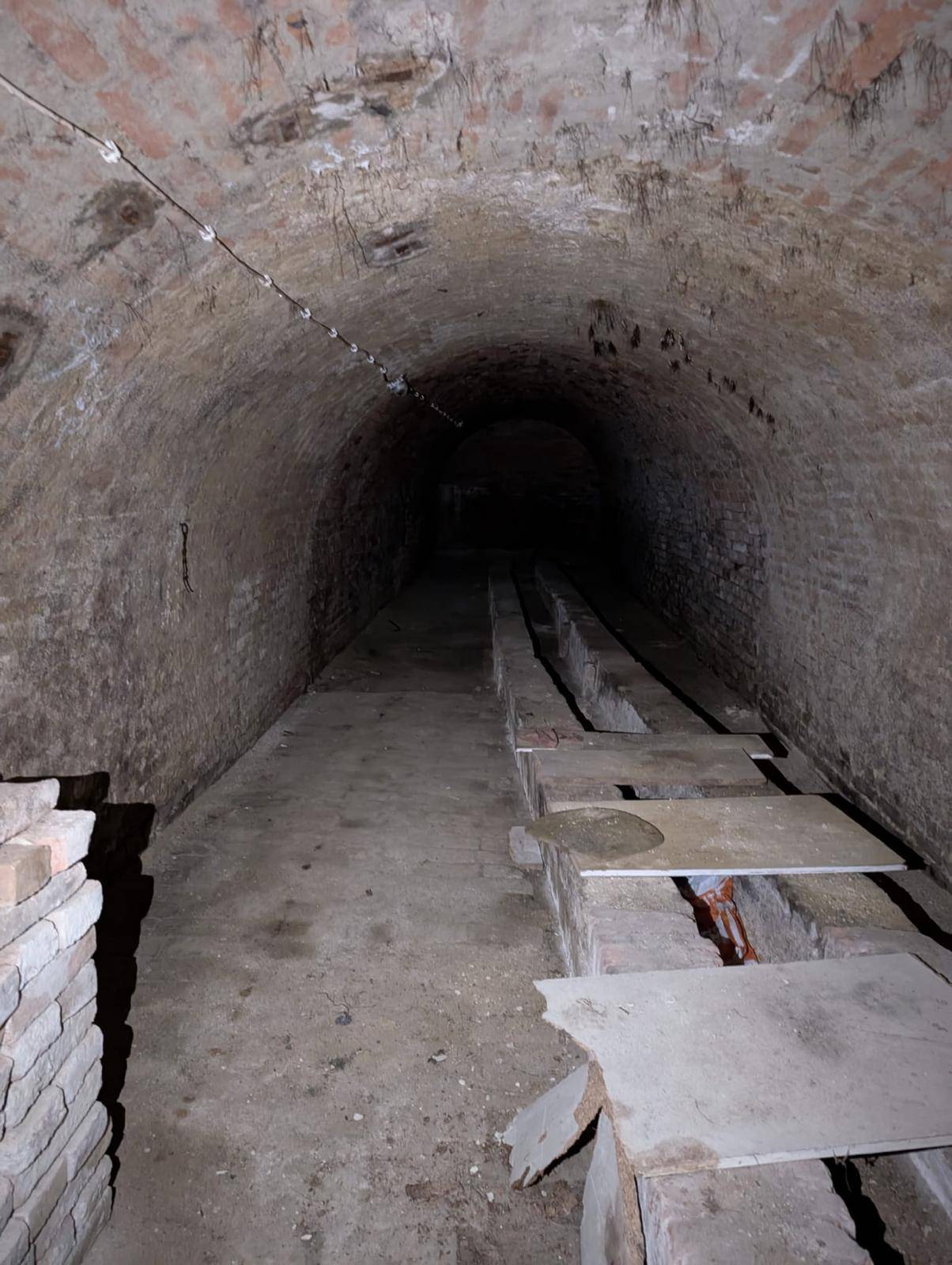 Weitläufiger, dunkler Gewölbekeller mit Ziegelwänden und einer langen Reihe von gemauerten Strukturen.