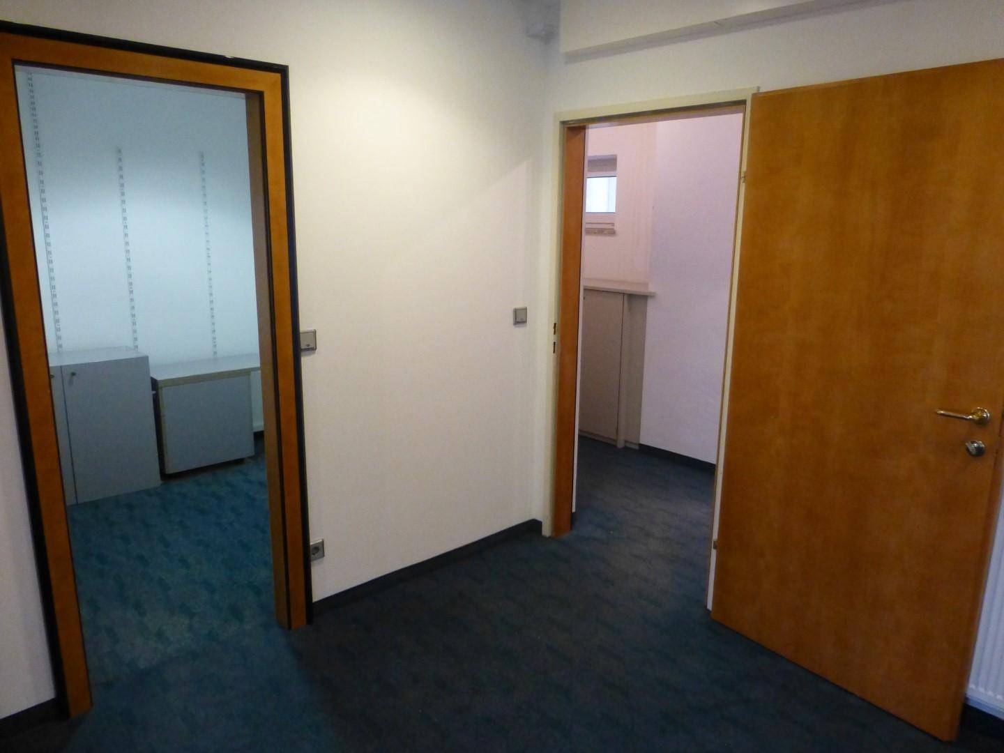 Blick durch zwei offene Holztüren in angrenzende Büroräume mit Teppichboden und einfacher Ausstattung.