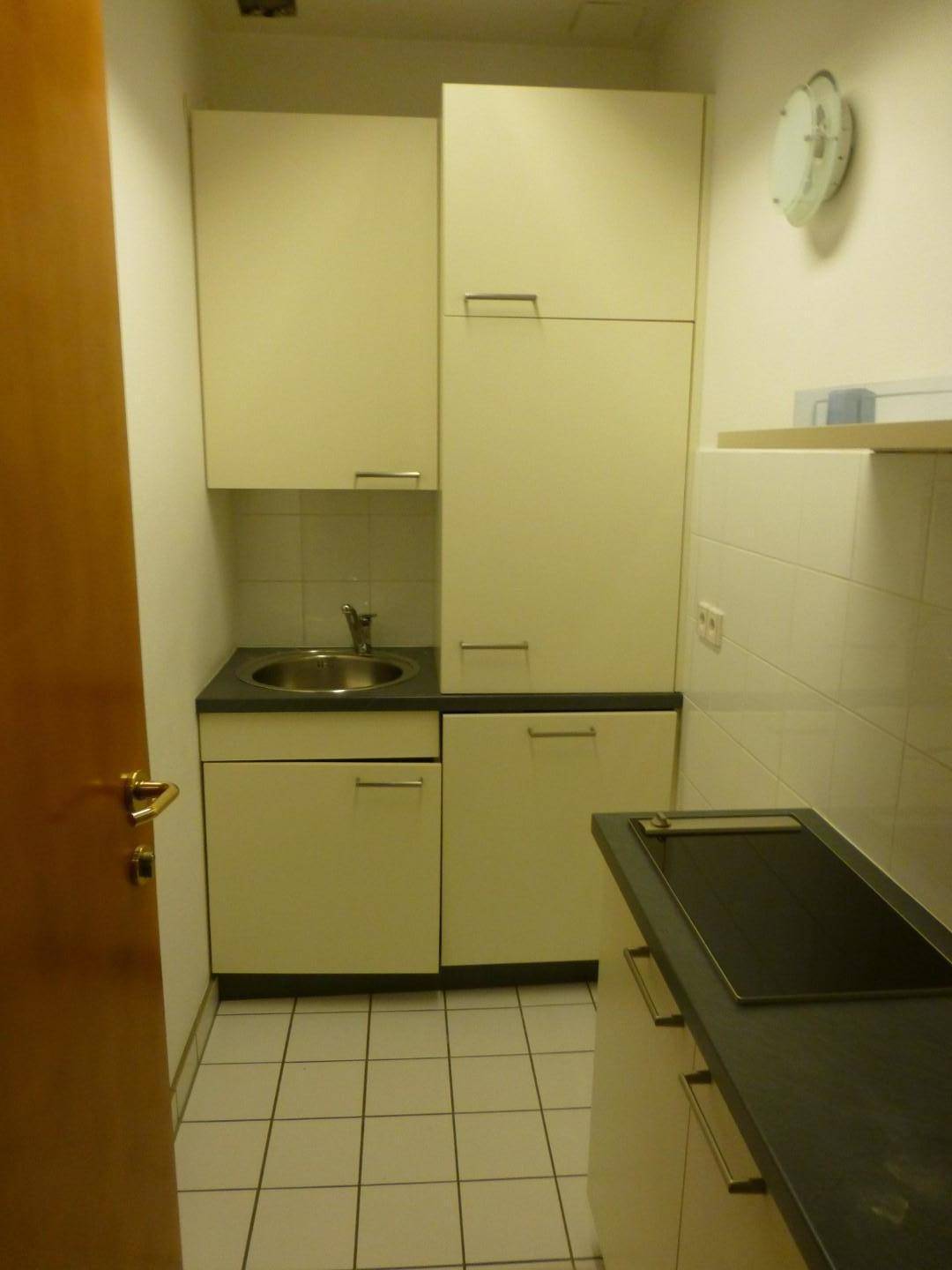 Kleine Küchenzeile mit cremefarbenen Schränken, Spüle und Kochfeld, ideal für eine Büroküche.