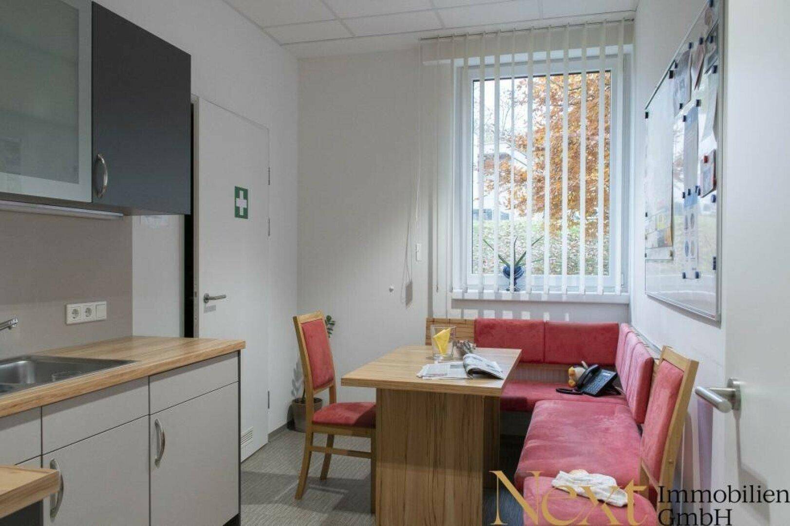 Kleine Küchenzeile mit Essbereich, roter Sitzbank und Fenster mit Blick nach draußen.