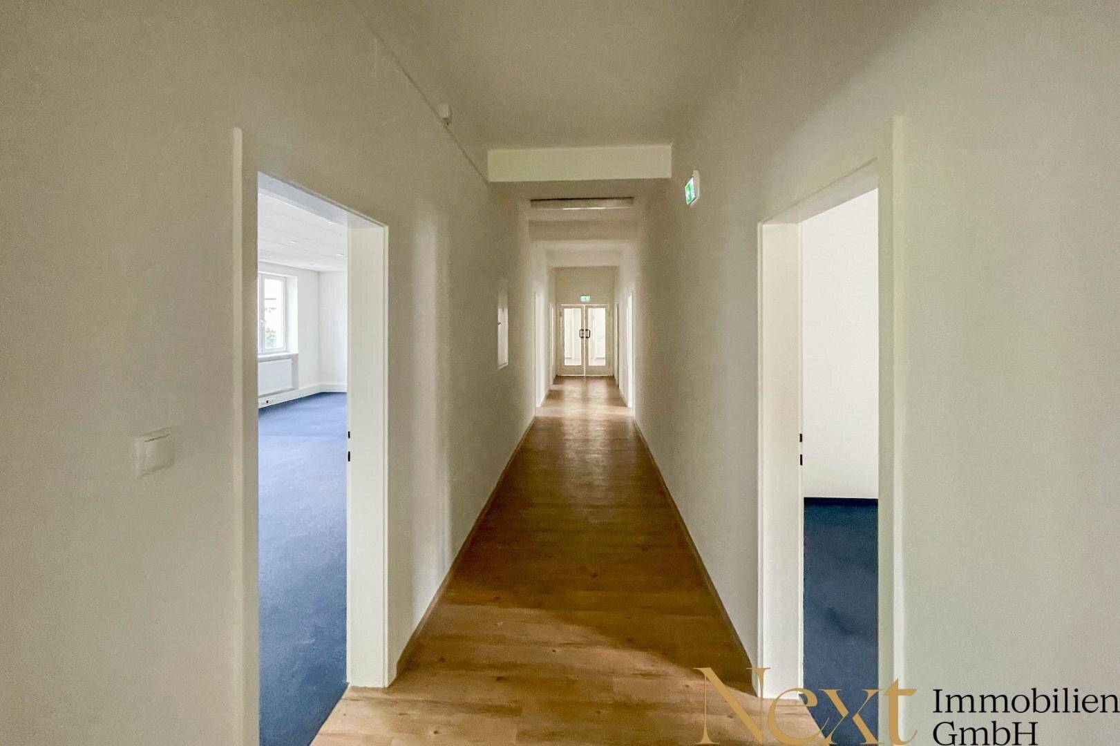 Langer, heller Flur mit Holzboden und Türen zu verschiedenen Büroräumen, gut beleuchtet.