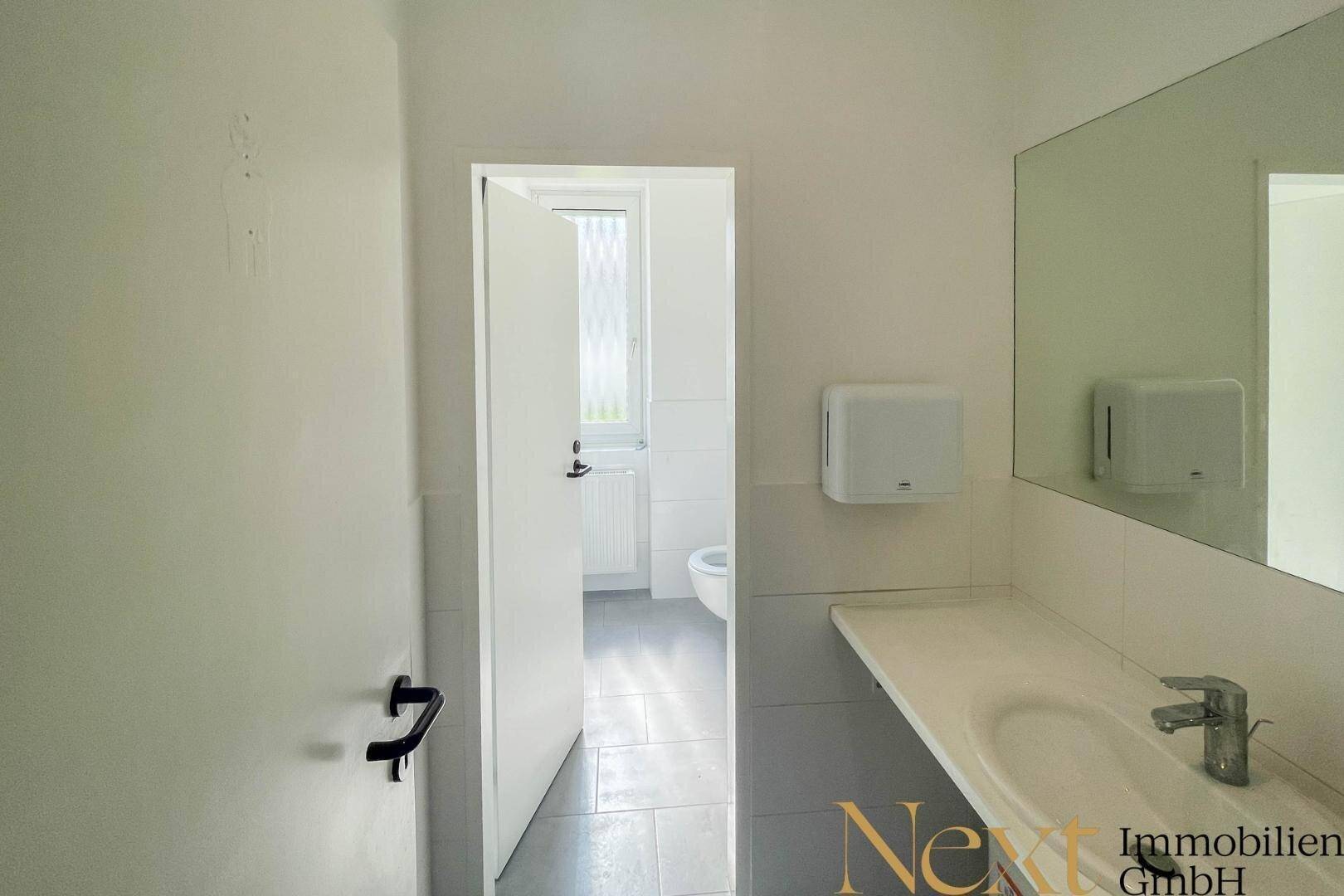 Helle Toilette mit Waschbecken, Spiegel und Fliesenboden, sauber und funktional gestaltet.