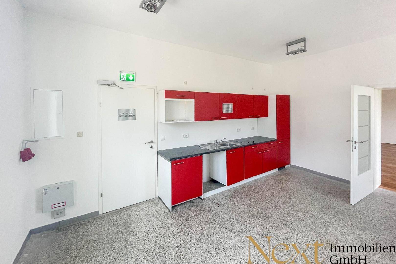 Funktionale Küchenzeile mit roten Schränken und Spüle, ideal für Pausenräume oder kleine Büros.