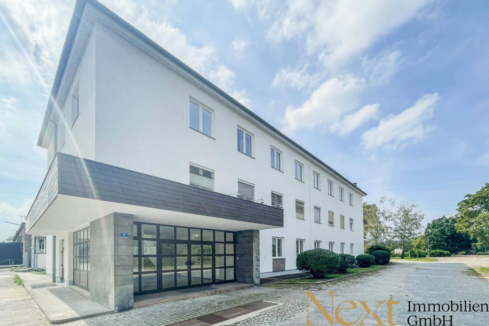 Modernes Bürogebäude mit weißer Fassade, großen Fenstern und einem überdachten Eingangsbereich.