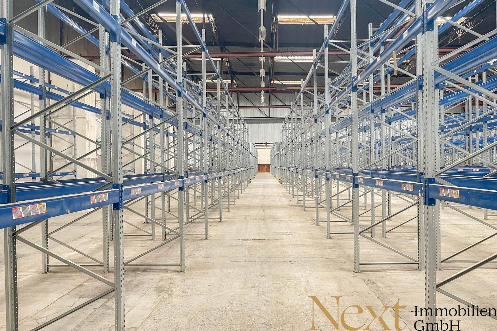 Langer Gang in einer Lagerhalle mit hohen, blauen Regalsystemen, optimiert für effiziente Lagerung.