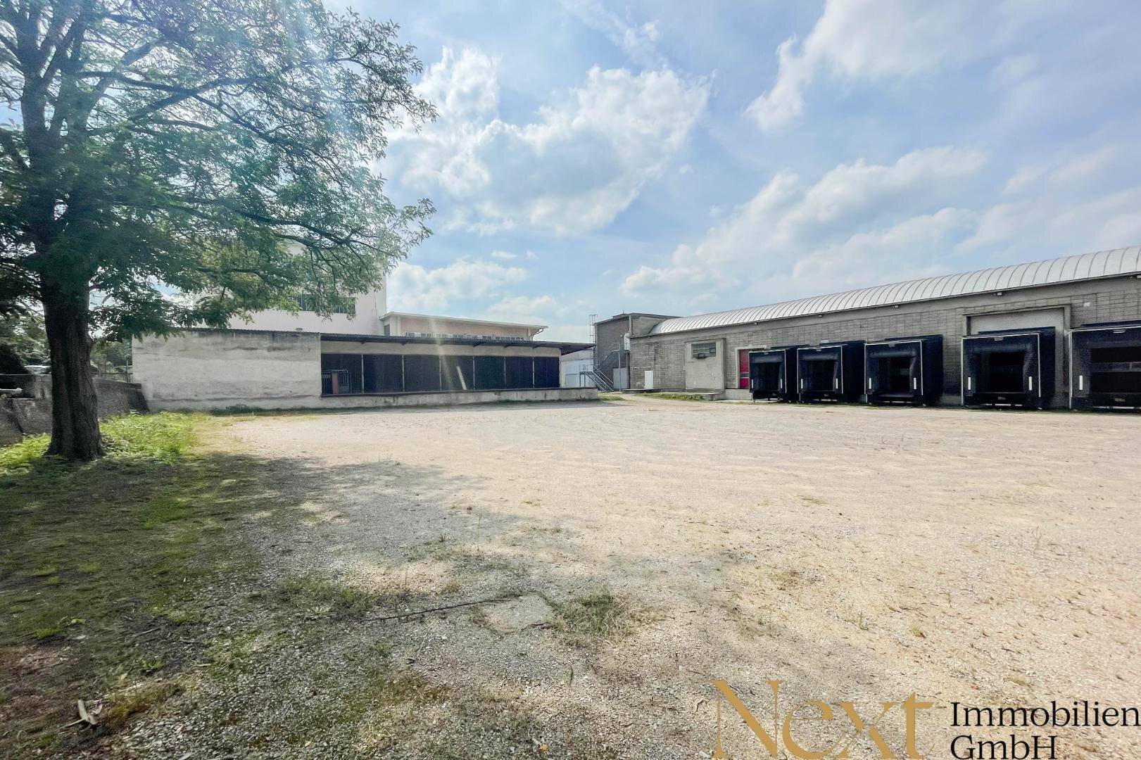 Gesamtansicht des Industriegebäudes mit großem Schotterparkplatz und umliegender Grünfläche.