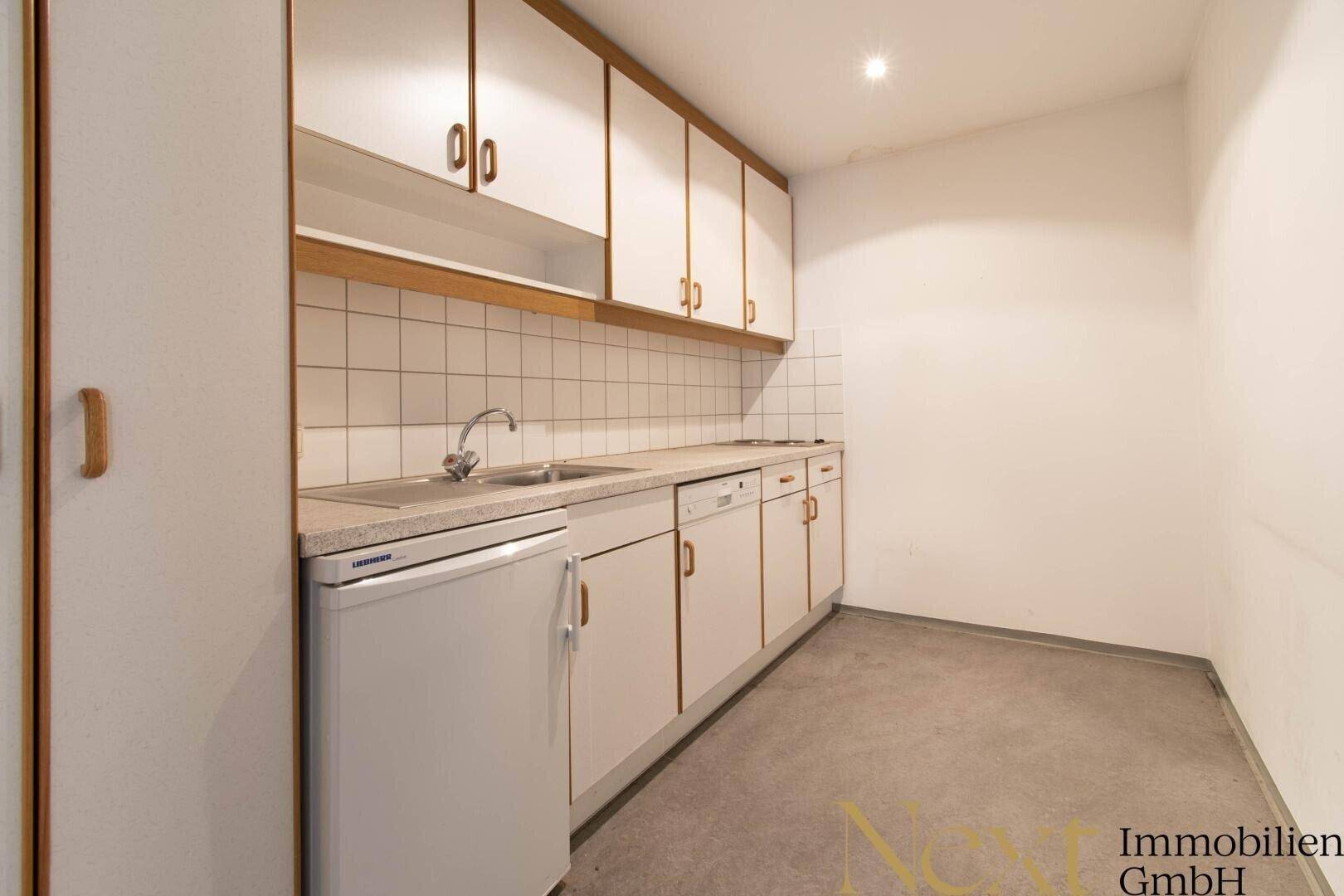 Funktionale Einbauküche mit weißen Schränken, Spüle, Kühlschrank und Fliesenrückwand in gutem Zustand.