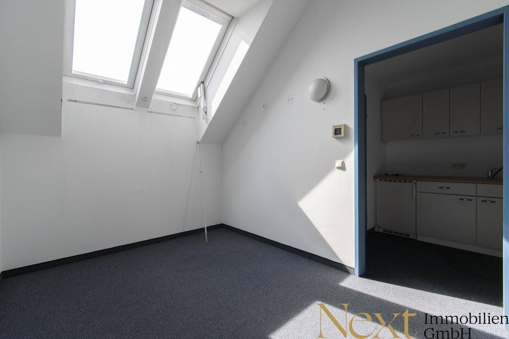 Kleinerer Büroraum im Dachgeschoss mit Teppichboden und Dachfenstern, angrenzend an eine Küchenzeile.