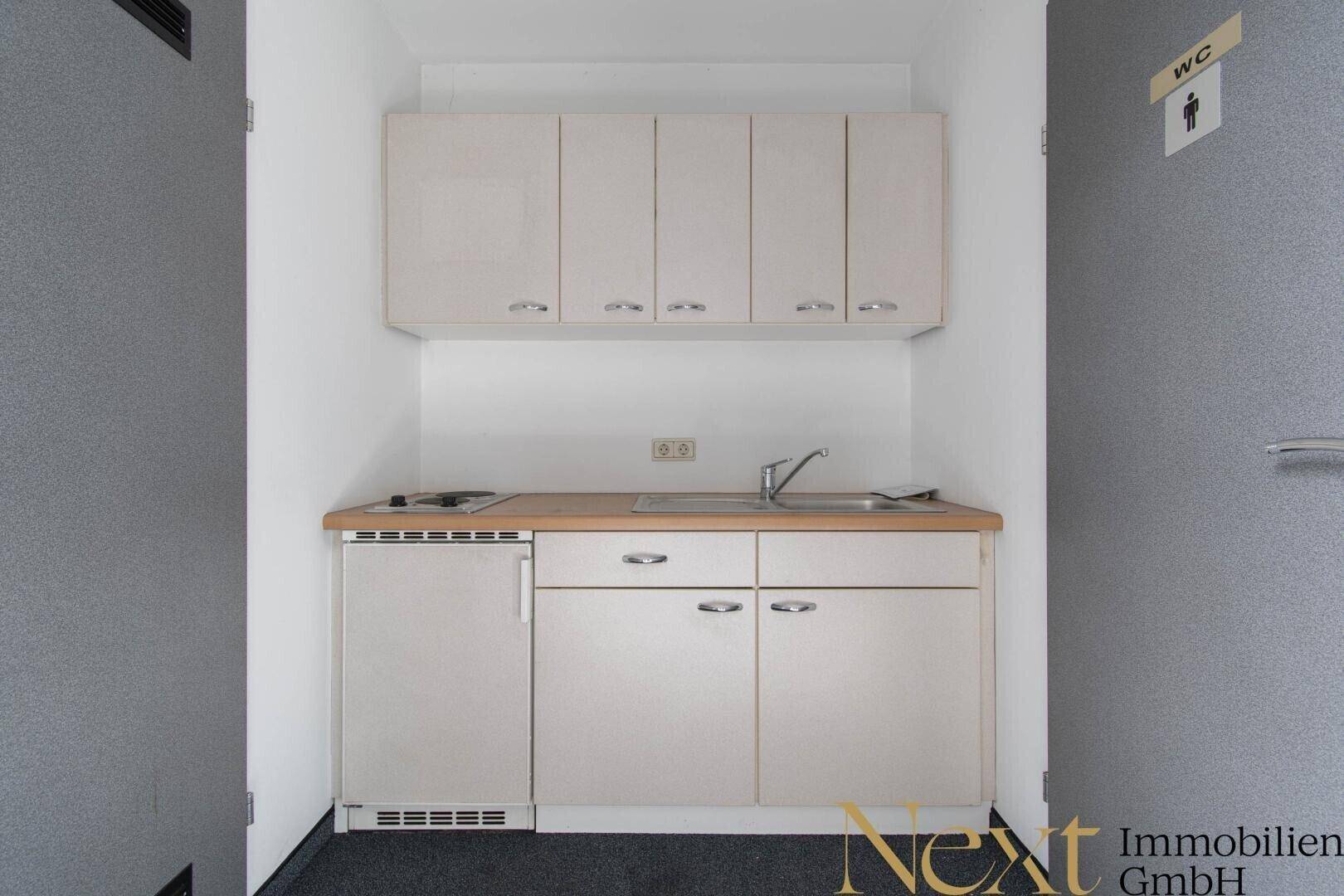 Kompakte Küchenzeile mit Spüle, Kochfeld, Kühlschrank und Holz-Arbeitsplatte, ideal für kleine Räume.