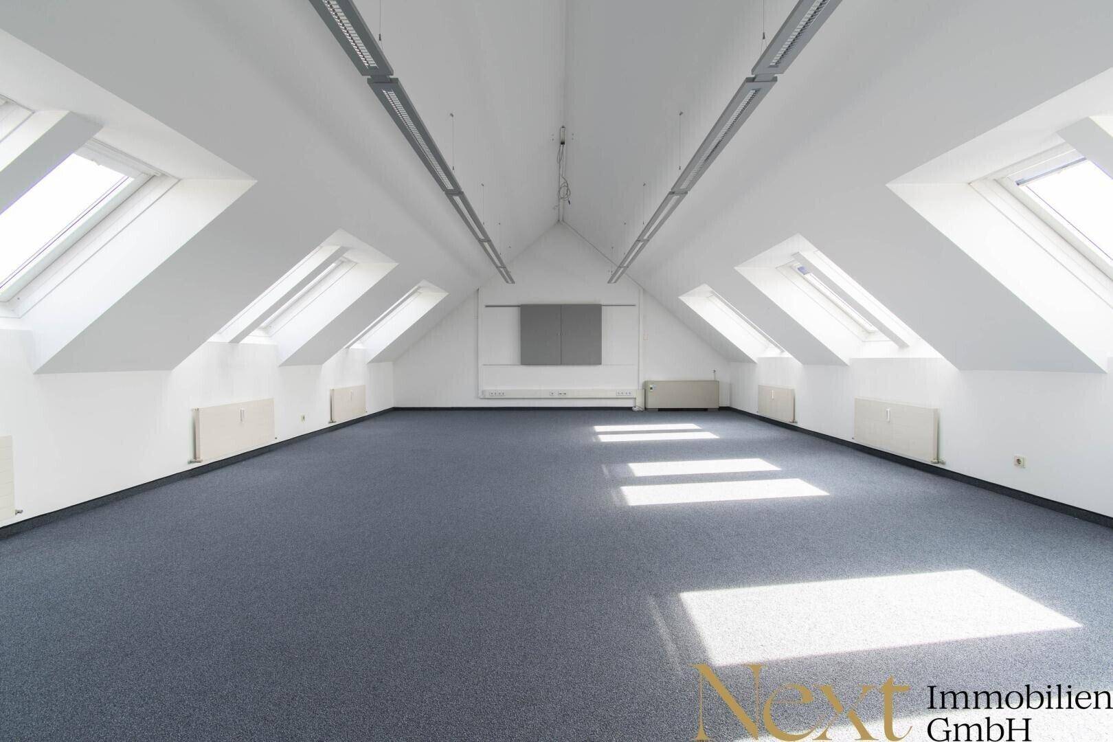 Großer, offener Büroraum im Dachgeschoss mit Teppichboden, vielen Dachfenstern und viel Tageslicht.